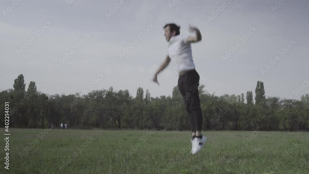Wide shot of young break dancer dancing on green summer meadow. Portrait of confident brunette Caucasian man training dance outdoors. Lifestyle and hobby concept. Wide shot of young break dancer dancing on green summer meadow. Portrait of confident brunette Caucasian man training dance outdoors. Lifestyle and hobby concept.