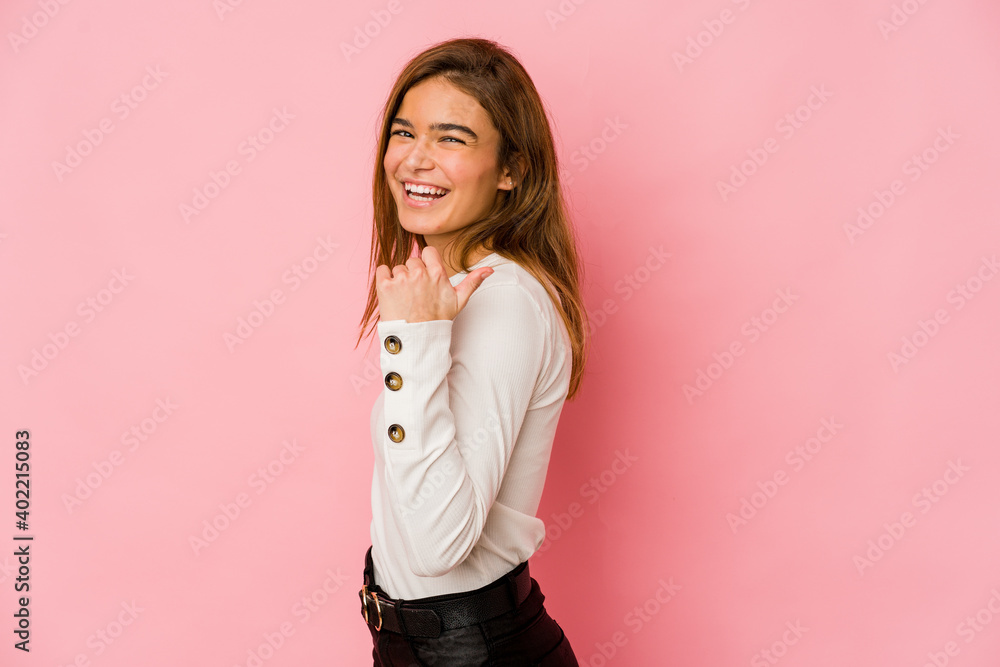 Young skinny caucasian teenager girl points with thumb finger away, laughing and carefree.