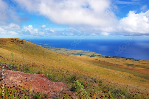 Panoramic view from the slopes of the Terevaka Volcano on Easter Island  showing green vegetation and the ocean against a blue sky.