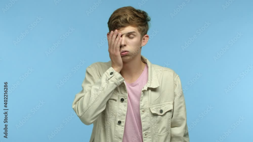 Slow motion of skeptical man facepalm and shake head, staring at camera bothered and annoyed, standing over blue background Slow motion of skeptical man facepalm and shake head, staring at camera bothered and annoyed, standing over blue background