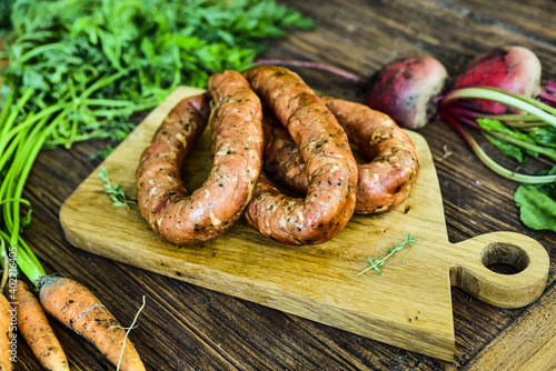 Sausage served on an oak board among vegetables from the home garden.