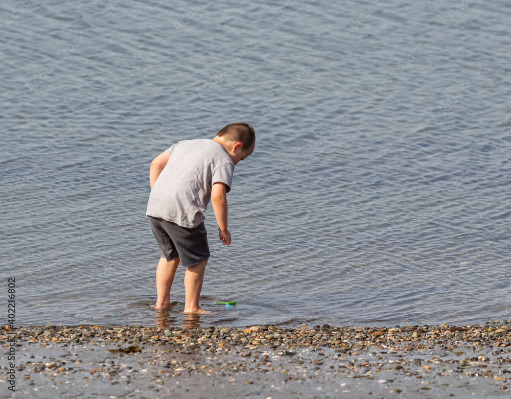 Child playing outdoors at the sea, a boy intering into the water.