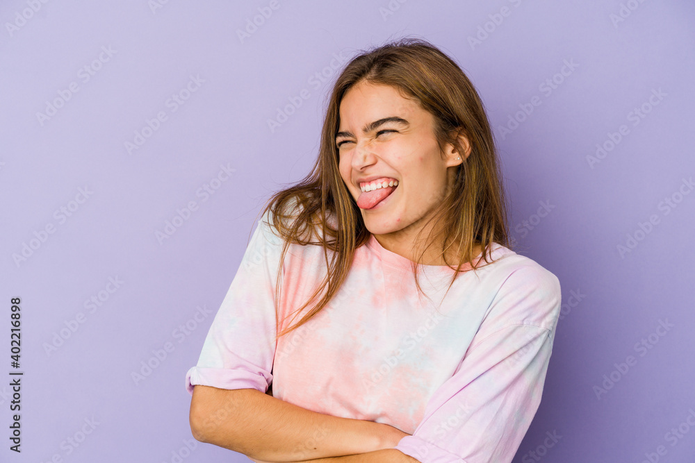 Fototapeta premium Young skinny caucasian girl teenager on purple background funny and friendly sticking out tongue.