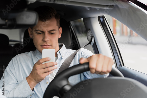 young man chatting on smartphone while driving car, blurred foreground.