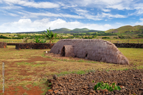 Fotografía Old Rapa Nui thatch-roofed house at the ceremonial center of Vaihu, on Easer Island, against a blue sky covered by white clouds