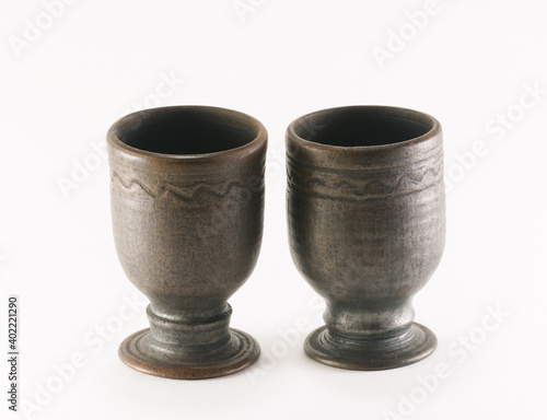 Two empty ceramic cups for alcohol and various herbal infusions are highlighted on a white background. The glasses are decorated with a simple wavy pattern. © Andrey