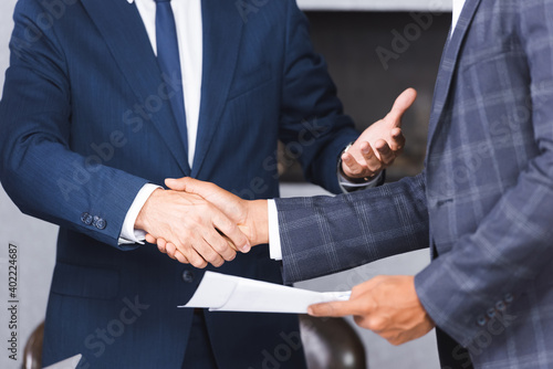 Cropped view of african american businessman holding documents and shaking hands with colleague.
