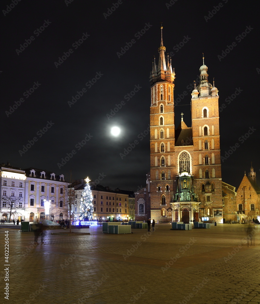 Night cityscape of Krakow old town, saint marys church, Christmas tree decorates main market square, full moon