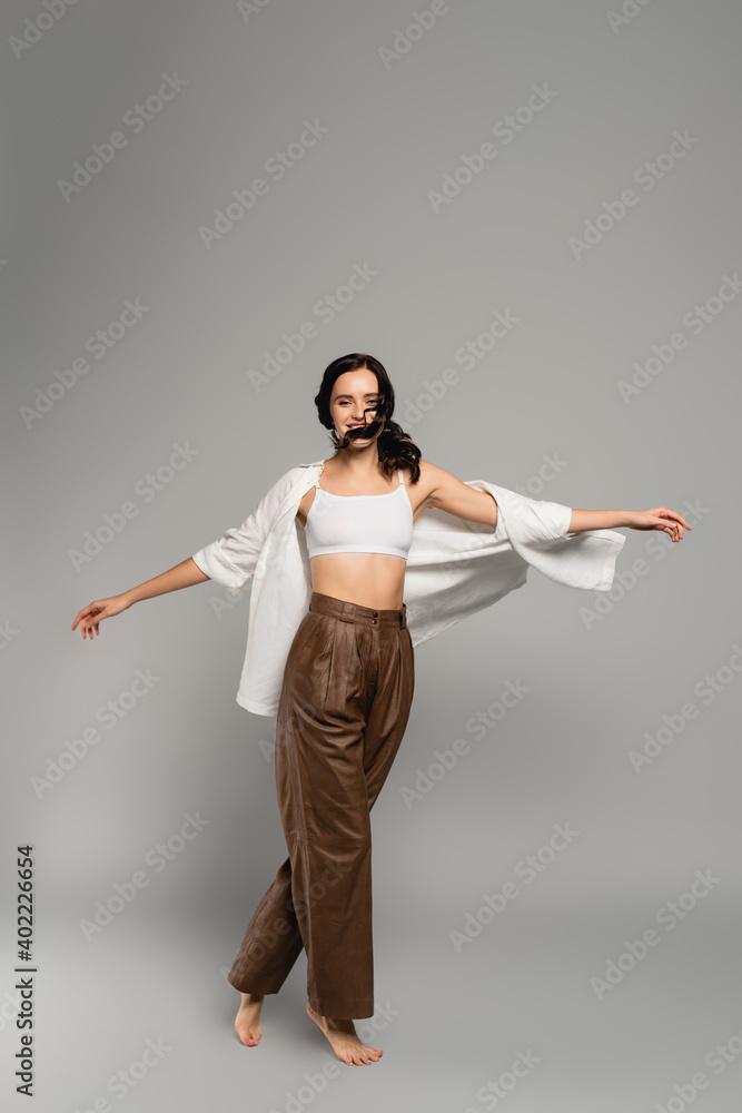 Full length of woman with outstretched hands looking at camera while turning round on grey Full length of woman with outstretched hands looking at camera while turning round on grey