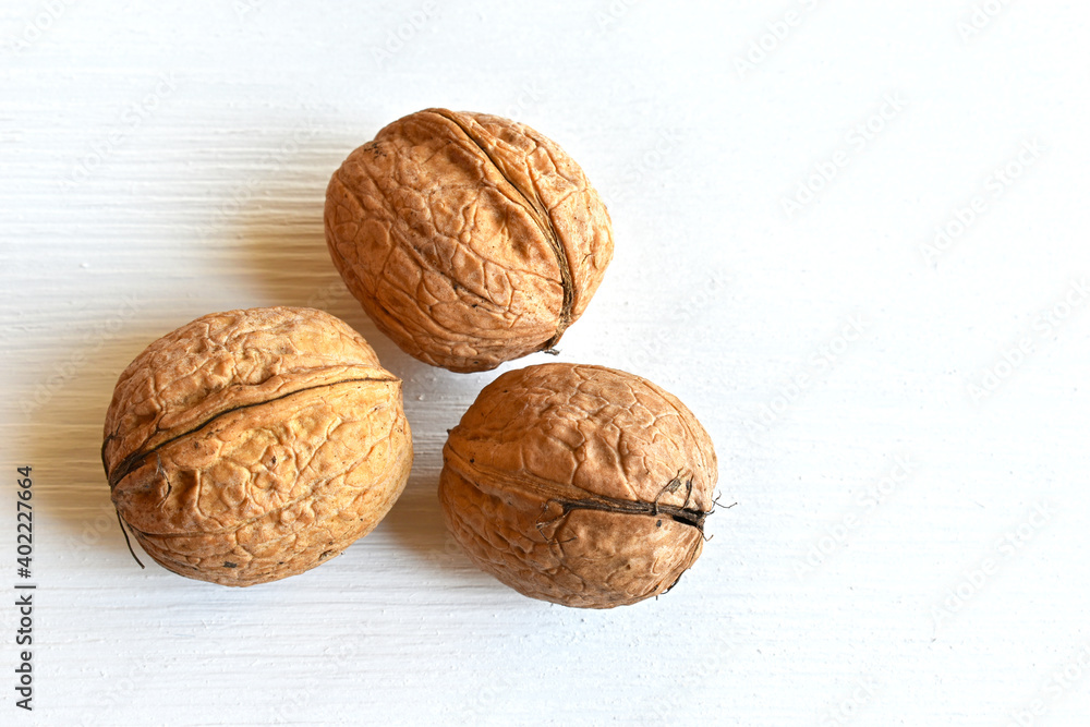Walnuts (Juglans regia) in shell on white wooden background, close-up, top view. Walnuts (Juglans regia) in shell on white wooden background, close-up, top view.