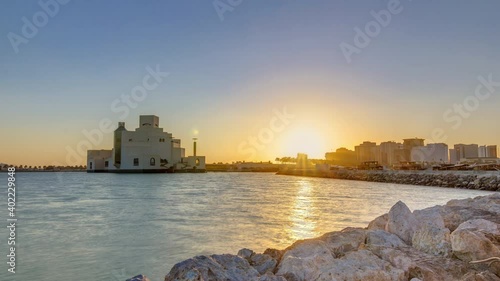 Doha Harbor with passing fishing boats during sunrise timelapse with museum on background. Doha, Qatar, Middle-East. Stones on foreground. photo