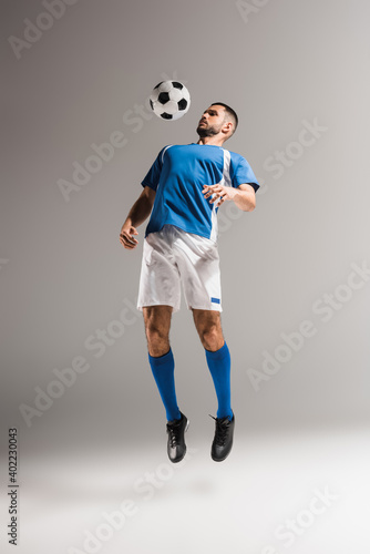 Fototapeta Naklejka Na Ścianę i Meble -  Sportsman jumping near football while training on grey background