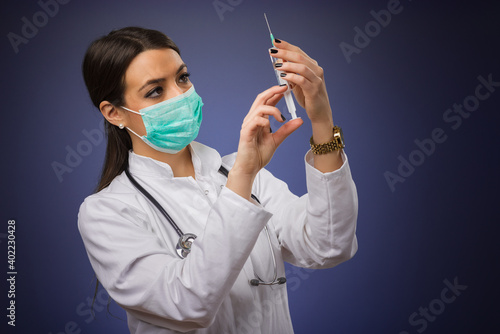 Young female doctor with stethoscope and face mask holding COVID-19 vaccine. Medicine student holding virus immunization vaccine. Healthcare, medical and cure concept