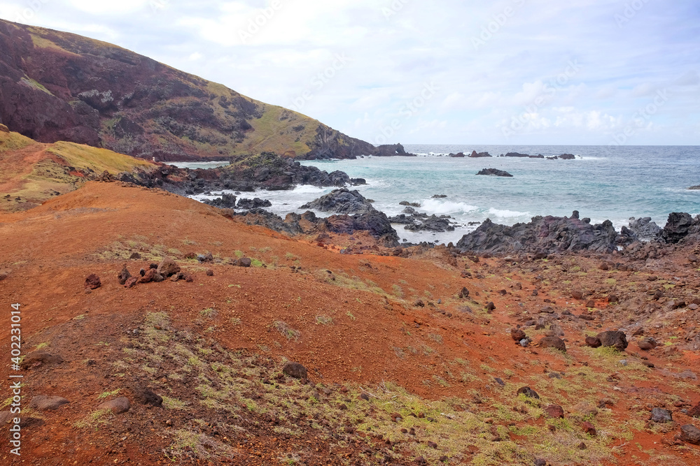 Small beach on the coast of Easter Island, covered by red volcanic dust, against a blue sky with white clouds. Small beach on the coast of Easter Island, covered by red volcanic dust, against a blue sky with white clouds.
