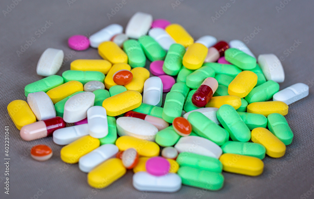Heap of multi-colored pills and capsules on gray background . Shallow focus Heap of multi-colored pills and capsules on gray background . Shallow focus