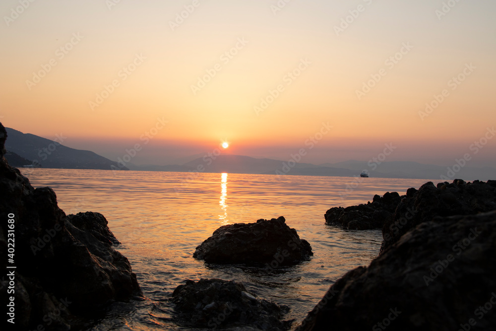 Sunrise / sunset over the sea, rocks and cliffs come out of the water with reflections of warm colors, golden hour.
