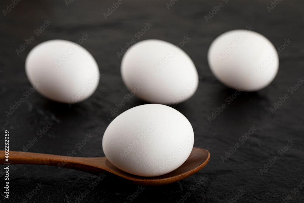 Raw white eggs and wooden spoon on black background Raw white eggs and wooden spoon on black background