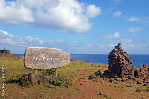 Wooden sign at the entrance of the Ana Kakenga cave, on Easer Island - Rapa Nui, against the ocean and a blue sky covered by white clouds. photo