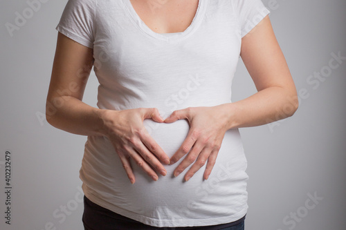 Pregnant woman forms a heart with hands in front of baby belly