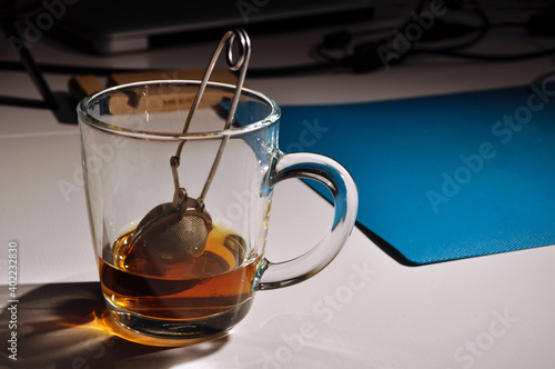 Stainless steel tea infuser in glass mug, cup of tea on a table. Half-finished, selective focus.