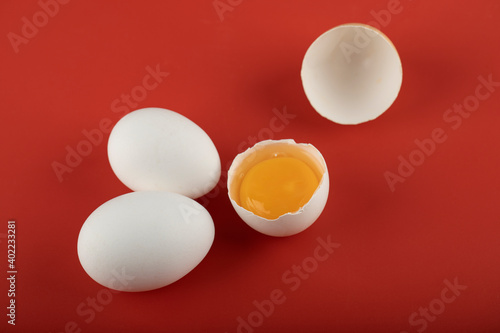 Broken and whole raw eggs on red background