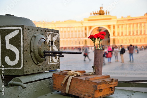Red carnations in a gun case and box of shells at a small Soviet amphibious tank T-38 in the background of the Headquarters ' Arch