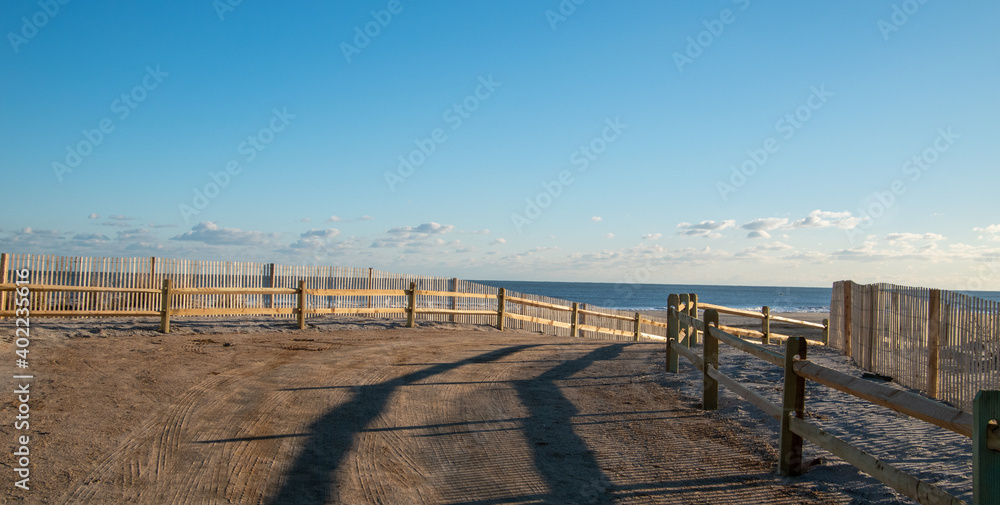 Curved sandy path to the ocean and beach lines with a wooden split rail fence and an erosion slat fence