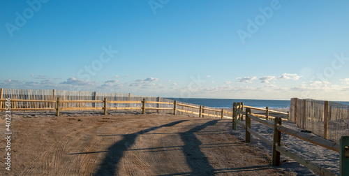 Curved sandy path to the ocean and beach lines with a wooden split rail fence and an erosion slat fence