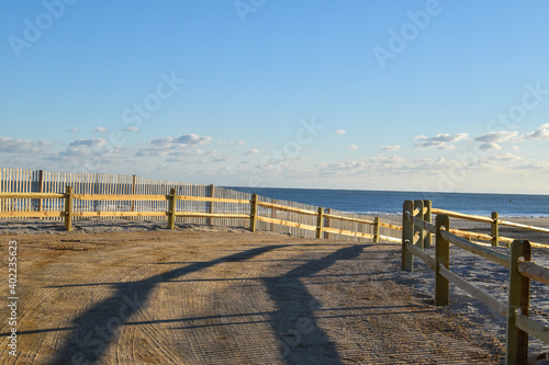 Curved sandy path to the ocean and beach lines with a wooden split rail fence and an erosion slat fence
