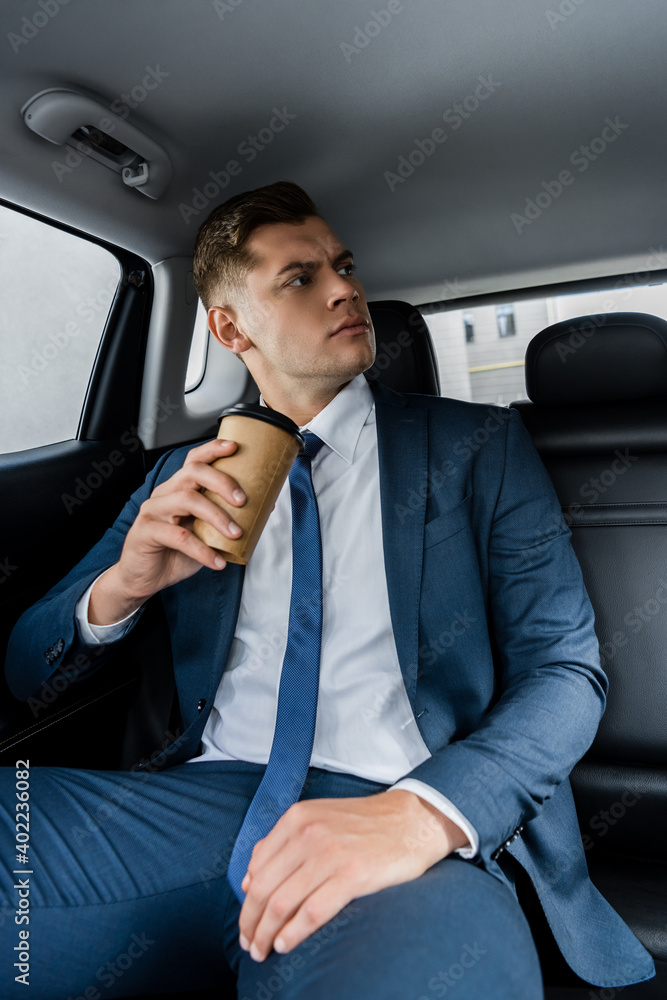 Confident businessman holding coffee to go on back seat of car.