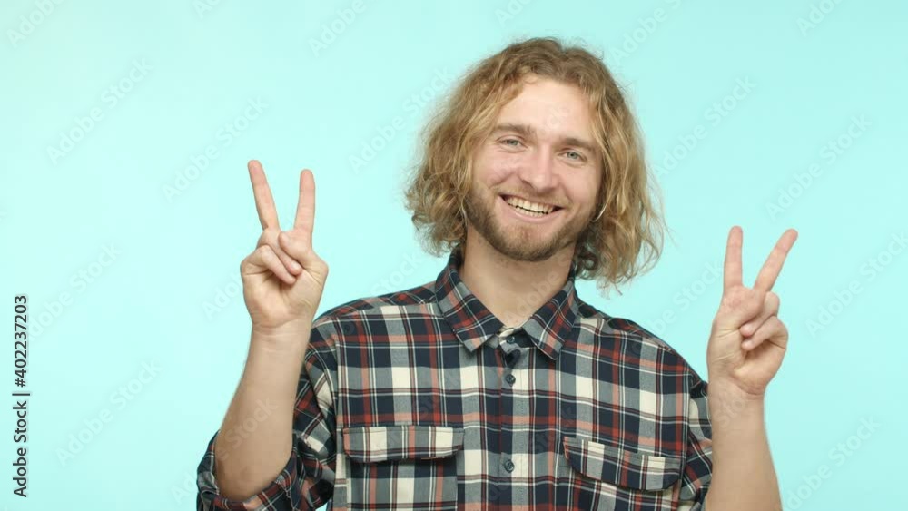 Slow motion of friendly handsome guy with blond wavy hair and beard, express peaceful and positive attitude, showing peace signs and smiling happy, standing over turquoise background Slow motion of friendly handsome guy with blond wavy hair and beard, express peaceful and positive attitude, showing peace signs and smiling happy, standing over turquoise background