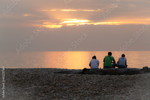 Fotografie Young people sit by the sea and watch the sunset