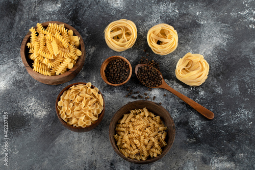 Dry pasta and black pepper grains on marble background