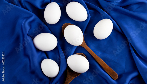 Photos Bunch of raw eggs with wooden spoon on blue sateen cloth