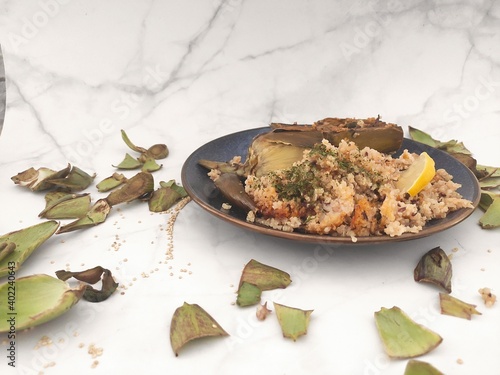 A top view of an healthy lunch, artichokes in a blue plate, white marble top and a side of quinoa