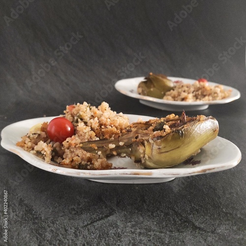 Two ocal plates of meal composed by artichoke, baked quinoa and cherry tomatoes photo