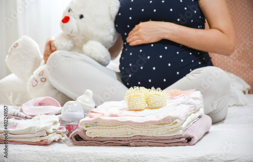 Pregnant woman is packing baby clothes for going to maternity hospital. Woman looking baby dress