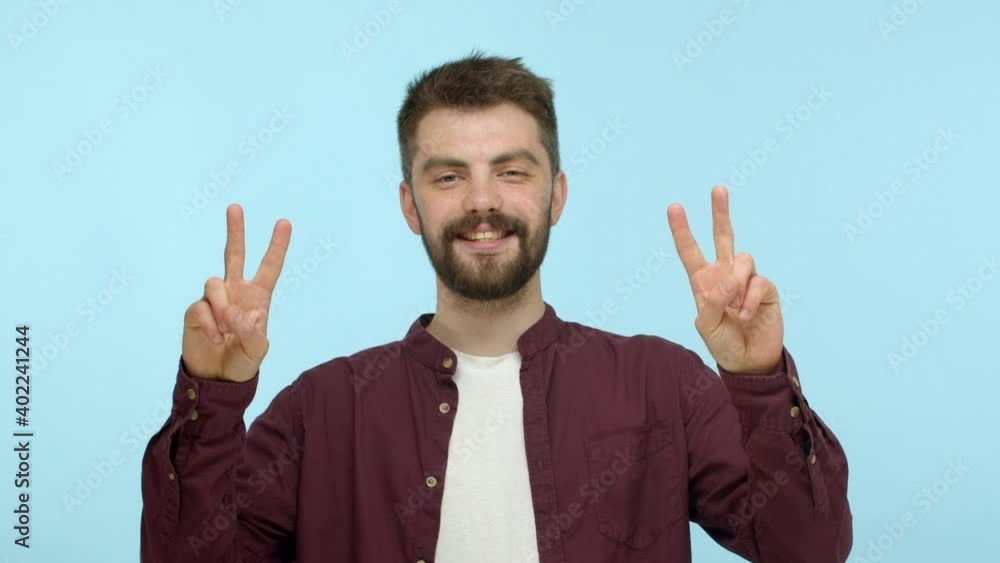 Slow motion of handsome and positive man with beard smiling friendly, showing peace signs and smiling, standing over turquoise background Slow motion of handsome and positive man with beard smiling friendly, showing peace signs and smiling, standing over turquoise background