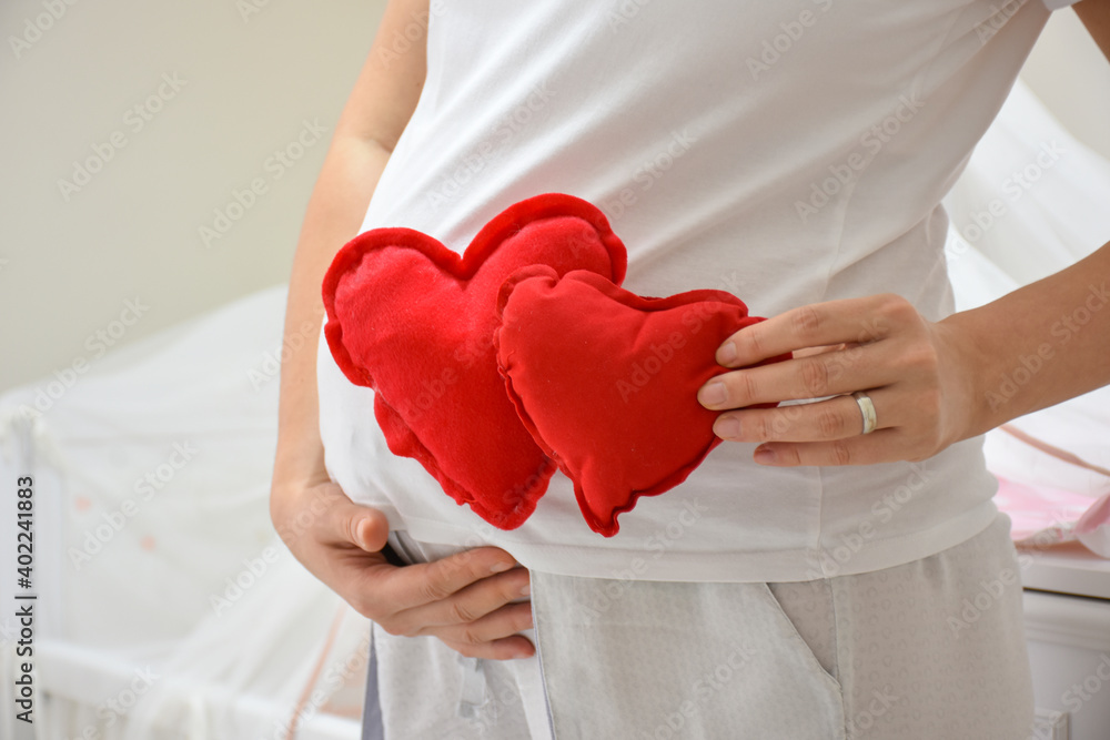 Pregnant woman holding a red heart sign. Pregnant woman put twins toy heart to her stomach on white background Pregnant woman holding a red heart sign. Pregnant woman put twins toy heart to her stomach on white background
