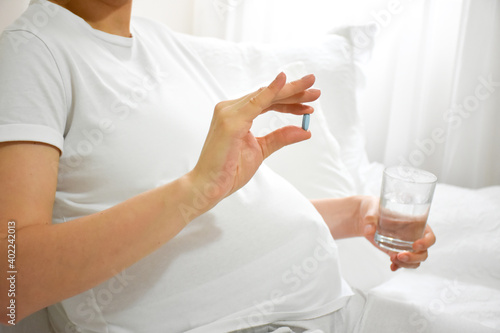 Close-up of Young pregnant woman holding glass of water and pill. Concept of pregnancy  health care  gynecology  medicine  and healthy lifestyle. Mother waiting of the baby. Nutritional supplements.