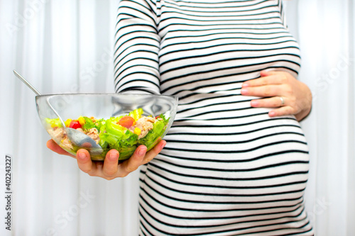 Cropped image of young hungry pregnant woman eating fresh tuna salad from glass bowl. Concept of healthy nutrition, vegetables and fish during pregnancy. Mother waiting baby. Omega 3 and vitamins.