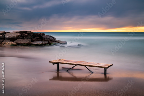 Long exposure of a picnic bench  on the rocky shores of Lake Ontario at sunrise © Moe Shirani