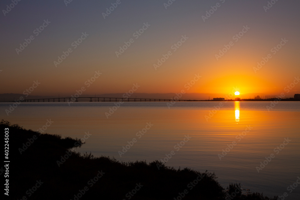 End of a summer day on the San Francisco East Bay, Coyote Point, California. Brilliant sunset setting over the bay with silhouette of bay bridge