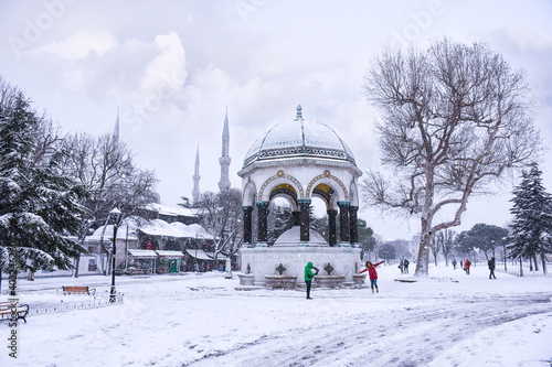 German Fountain in old Hippodrome, Istanbul, Turkey in winter day with snow, one tourist group walk around.