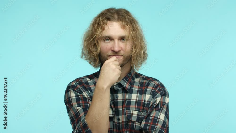 Slow motion of attractive european man with long blond hair, looking pensive and touching beard while thinking, pitching an idea, shouting excited and happy, standing over blue background
