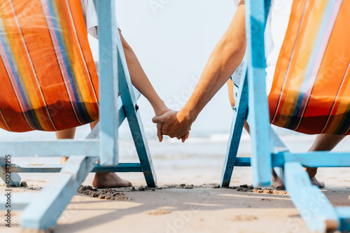 Couple of lovers sitting on beach chair holding hands on the beach in the morning.  Newlywed couple on a romantic vacation