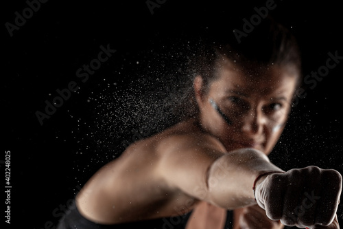 Kickboxer kirl with magnesium powder on her hands, punching with dust visible