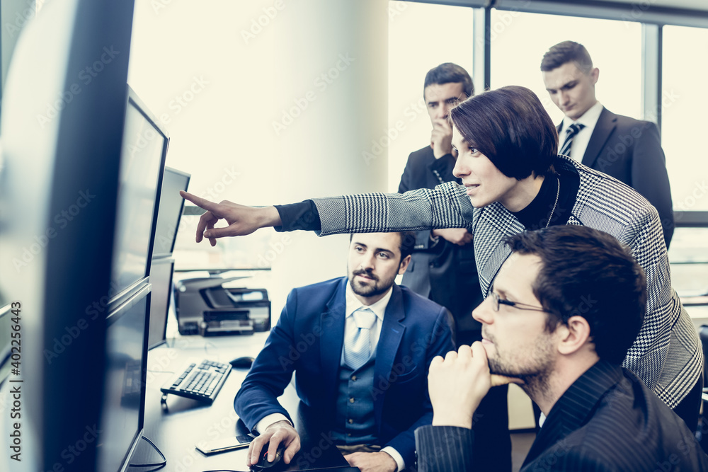 Fototapeta premium Business team looking at data on multiple computer screens in corporate office. Businesswoman pointing on screen. Business people trading online. Business, entrepreneurship and team work concept.