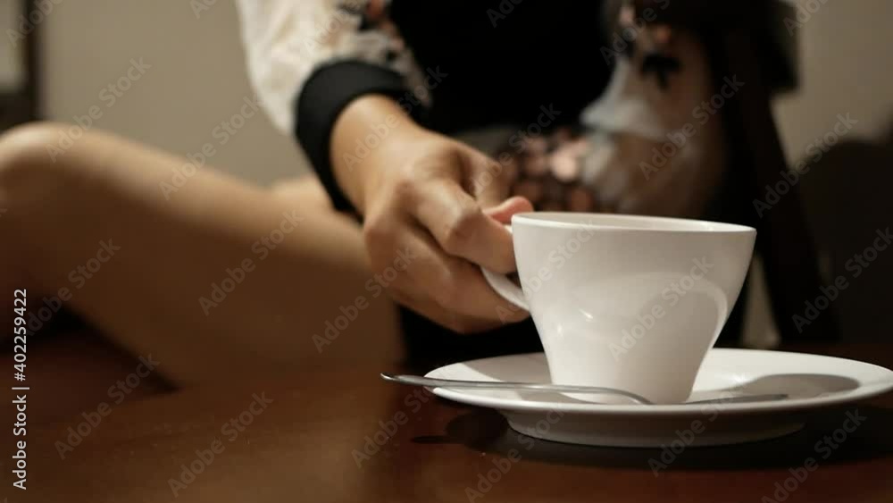 Young woman sitting on wooden chair at home relaxing in her living room and drinking coffee or tea. Young woman sitting on wooden chair at home relaxing in her living room and drinking coffee or tea.