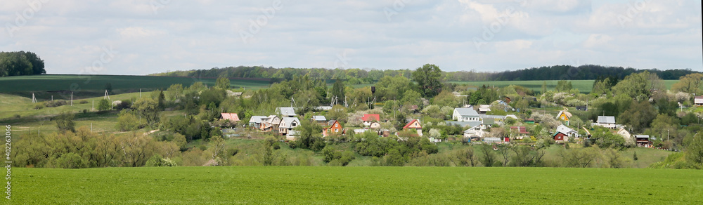 A lawn with green grass all the way to the horizon. Horizontal landscape of a flat field with fresh spring grass. Village, country houses, SNT, on the background of fields and trees. A lawn with green grass all the way to the horizon. Horizontal landscape of a flat field with fresh spring grass. Village, country houses, SNT, on the background of fields and trees.
